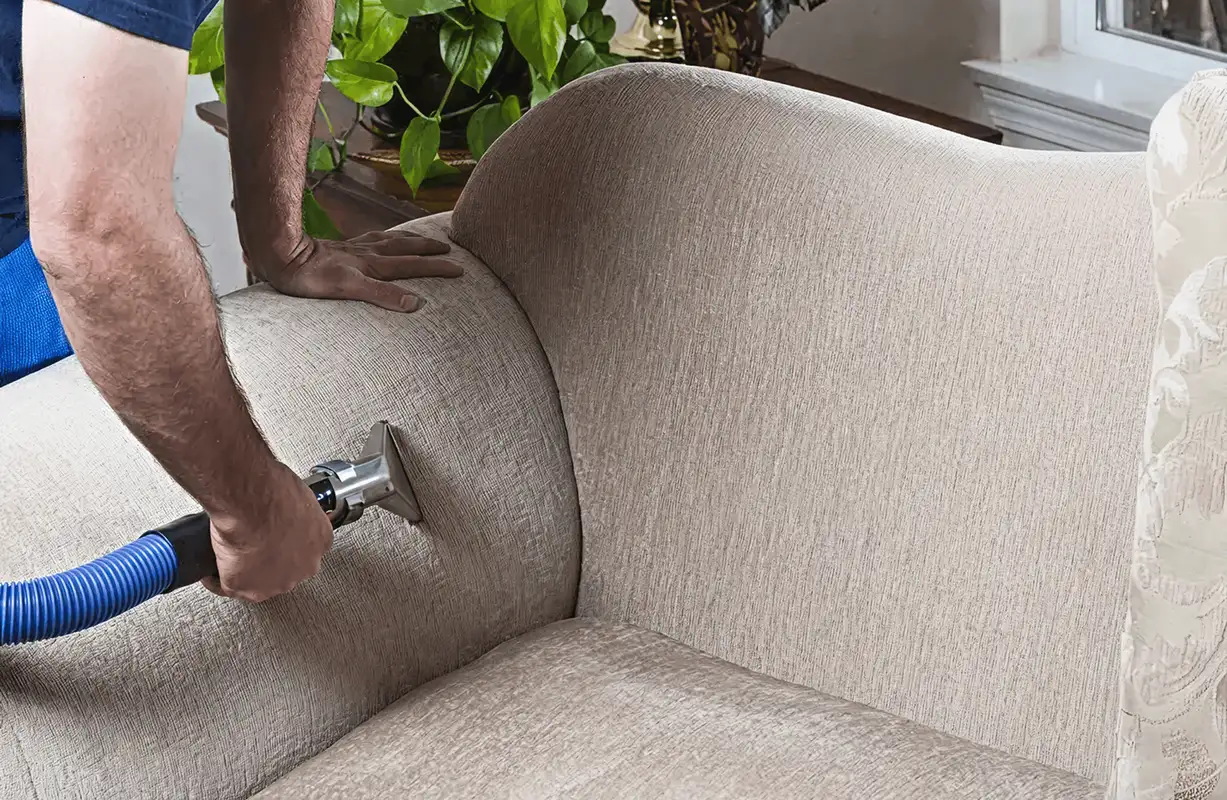 Professional upholstery cleaner deep-cleaning a fabric sofa with a handheld extraction tool and hose, Denver, CO.